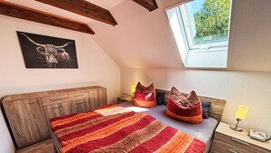 A bedroom with a sloped ceiling, a bed with a striped blanket, two bean bags, a bedside table with a lamp, and a framed picture on the wall. - Apartment Peters by Interhome (Esens)