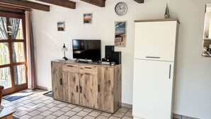 A room with a wooden cabinet, a television, a clock, and a refrigerator. - Apartment Peters by Interhome (Esens)