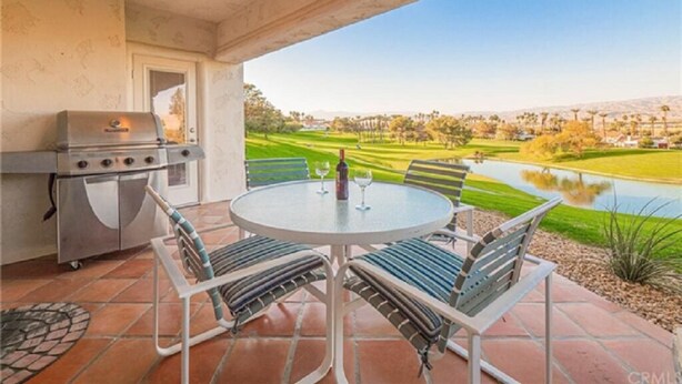 Un patio exterior con una mesa redonda y sillas, una parrilla y vistas a un campo de golf y un lago.