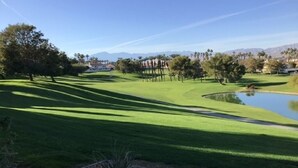 Un campo de golf con un estanque, árboles y cielo despejado.