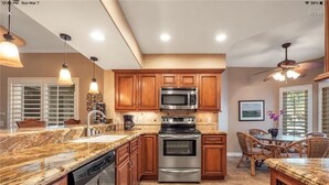Una cocina moderna con encimeras de granito, electrodomésticos de acero inoxidable, armarios de madera y un comedor con sillas de mimbre.