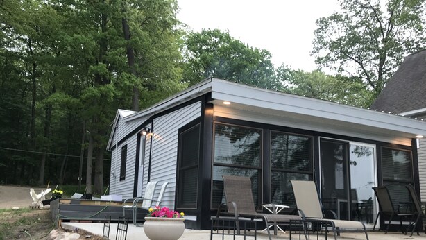 A modern house with a patio area featuring outdoor furniture and a large planter with flowers. - Cozy Cottage on Baptist Lake Just North of G.R. (Sand Lake)