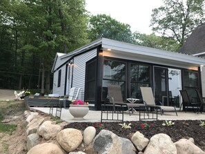 A modern house with a patio area featuring outdoor furniture and a large planter with flowers. - Cozy Cottage on Baptist Lake Just North of G.R. (Sand Lake)