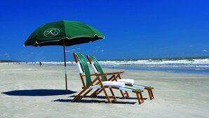 Een strand met een groene parasol en twee houten ligstoelen.