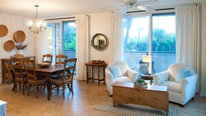 Een ruime woonkamer met een eethoek, met een houten tafel, stoelen, een bank en een plafondventilator.