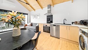 Eine moderne Küche mit Holzbalkendecke, einem Essbereich mit Tisch und Stühlen, einer Couch und einer Waschmaschine.