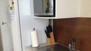Een kleine keuken met een koelkast, een magnetron, een spoelbak en een messenblok.