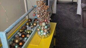 Een kamer met een gele dressingkast, een glazen pot gevuld met kerstversieringen en een raam met gordijnen.