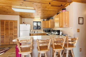 Eine Küche mit Holzausstattung, einem Kühlschrank, einer Mikrowelle und einem Essbereich mit Holztischen und -stühlen.