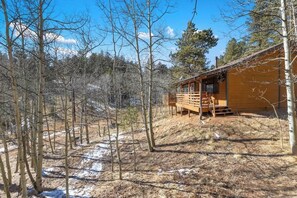 A cabin with a wooden deck, surrounded by trees and a hilly landscape. - Bear Foot Getaway - Secluded Cabin with Hot Tub! (Cripple Creek)