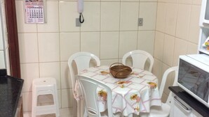 A small kitchen with a tiled backsplash, a wall-mounted clock, a calendar, a phone, a microwave, and a table with chairs. - Apartamento de um Quarto (RJ)