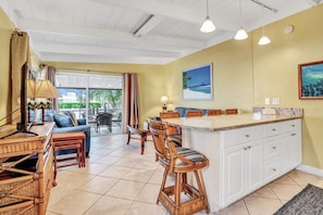A bright kitchen with a large island, white cabinets, and a view of the outdoors.