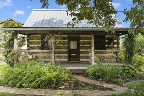 A rustic log cabin with a metal roof, a wooden front door, and a porch with a bench.