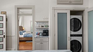 A compact hotel room with a bed, a kitchenette, a washing machine, and a bathroom. - Morning Glory | Newly Renovated | Pet-friendly (Fredericksburg)