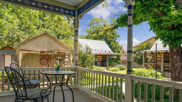 A wooden deck with a table and chairs, a covered area, and a view of surrounding buildings and trees. - Morning Glory | Newly Renovated | Pet-friendly (Fredericksburg)