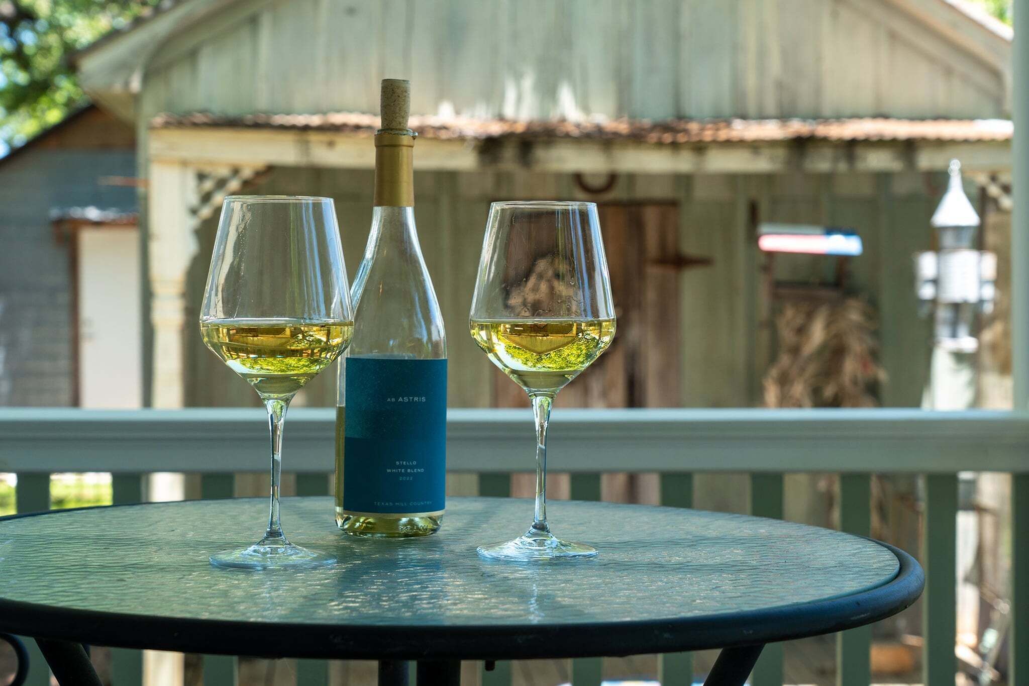 A bottle of white wine and two glasses on a round table with a view of a building in the background.