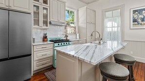 A kitchen with white cabinetry, a stainless steel refrigerator, a gas stove, and a marble island with stools. - Morning Glory | Newly Renovated | Pet-friendly (Fredericksburg)