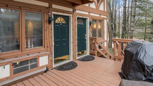 Eine Holzterrasse mit überdachter Grillgegend, eine Haustür mit Fenster und eine Treppe, die zu einer oberen Ebene führt.