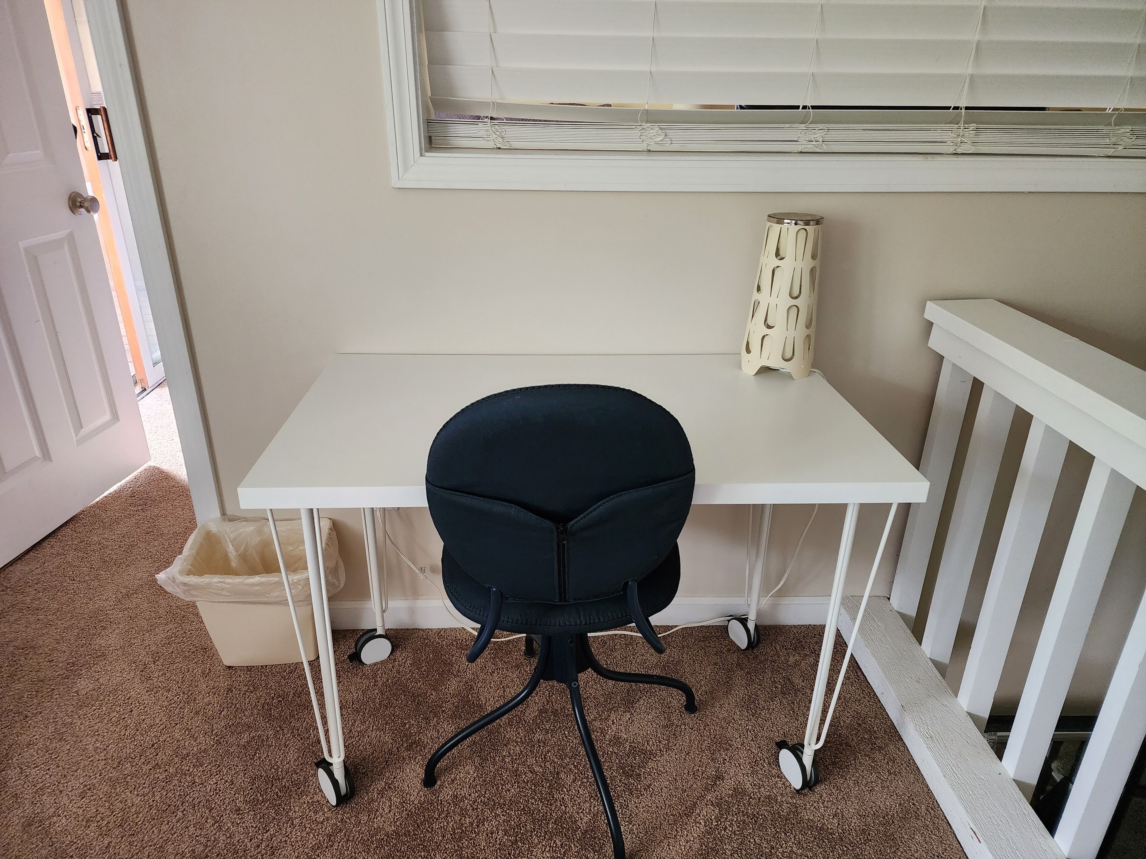 A small, white desk with a black office chair, a white radiator, and a white door in the background.