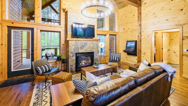 A cozy log cabin interior with a stone fireplace, leather sofa, and a television mounted above it. - Candy Apple Cabin- Stay 3 get 4th Night FREE (Broken Bow)