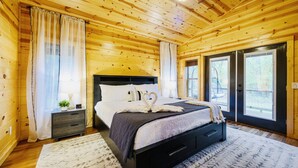 A wooden cabin bedroom with a bed, nightstand, and large windows. - Candy Apple Cabin- Stay 3 get 4th Night FREE (Broken Bow)