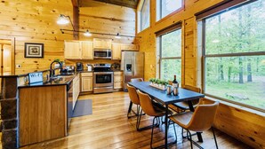 A wooden cabin interior with a kitchen, dining area, and large windows. - Candy Apple Cabin- Stay 3 get 4th Night FREE (Broken Bow)