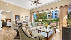 A spacious living room with a sofa, armchairs, and a coffee table. There is a dining area with a table and chairs, and a view of the outside through large windows. - Maui Resort Rentals: Honua Kai - 4 Total Bedrooms, Ground Floor, Steps to Pools, Beach, BBQs, Partial Ocean Views from Lawn Area! (Lahaina)