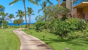 A pathway leading to a building with a view of the ocean. - Maui Resort Rentals: Honua Kai - 4 Total Bedrooms, Ground Floor, Steps to Pools, Beach, BBQs, Partial Ocean Views from Lawn Area! (Lahaina)