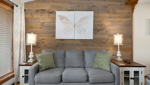 A grey sofa with two green pillows, flanked by two white bedside tables with lamps, against a wooden wall with a butterfly artwork above. - Notch★The Chic Retreat★Trailer Parking1Mi to SDC (Branson West)
