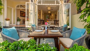 Een open terras met rieten meubels, een eettafel gedekt voor twee personen en uitzicht op het huis.