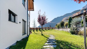 A modern building with a stone pathway leading to a door, surrounded by a well-maintained lawn and trees. - Modern Apartment "3 Weger" with Panoramic Mountain Views, Balcony, and Wi-Fi (Andrian)