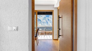 A hallway with a wooden door, a light switch, and a view of a mountainous landscape through a glass door. - Modern Apartment "3 Weger" with Panoramic Mountain Views, Balcony, and Wi-Fi (Andrian)