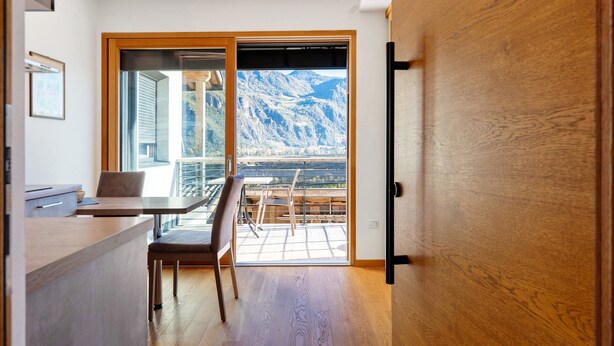 A modern interior with a dining area, a sliding glass door leading to a balcony with a mountain view. - Modern Apartment "3 Weger" with Panoramic Mountain Views, Balcony, and Wi-Fi (Andrian)