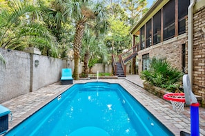 A rectangular swimming pool with a brick border, surrounded by a stone wall and lush greenery.