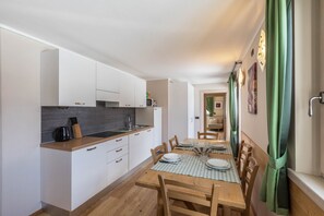 Une cuisine compacte avec des meubles blancs, un plan de travail en bois et un coin repas agrémenté d’une nappe à carreaux.