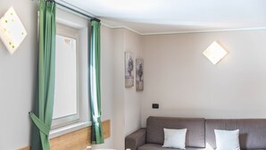 Um quarto com cabeceira de madeira, um sofá marrom com almofadas brancas, uma mesa de madeira e uma janela com cortinas verdes.