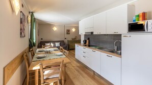 Uma cozinha compacta com armários brancos, micro-ondas e uma área de refeições com mesa e cadeiras de madeira.