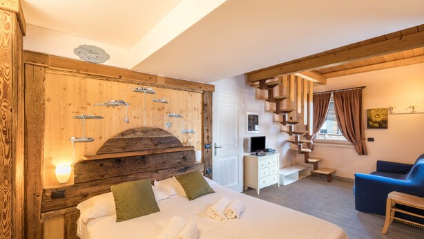Um quarto estilo cabana de madeira, com cama, almofadas, uma escrivaninha, uma cadeira e uma escada.