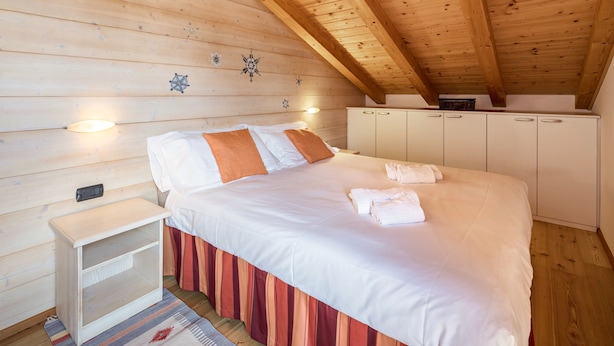 A bedroom with a wooden ceiling, a bed with white bedding, a nightstand, and a wardrobe.