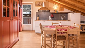 A wooden dining table with chairs, a kitchen with white cabinets, a stove, and a microwave.