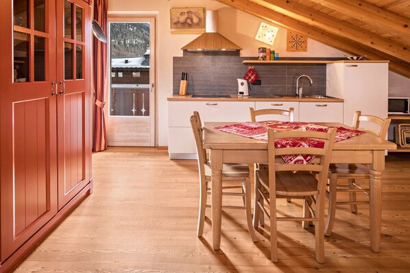 A wooden dining table with chairs, a kitchen with white cabinets, a stove, and a microwave.