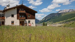 A two-story building with a balcony, surrounded by a grassy field and mountains in the background.