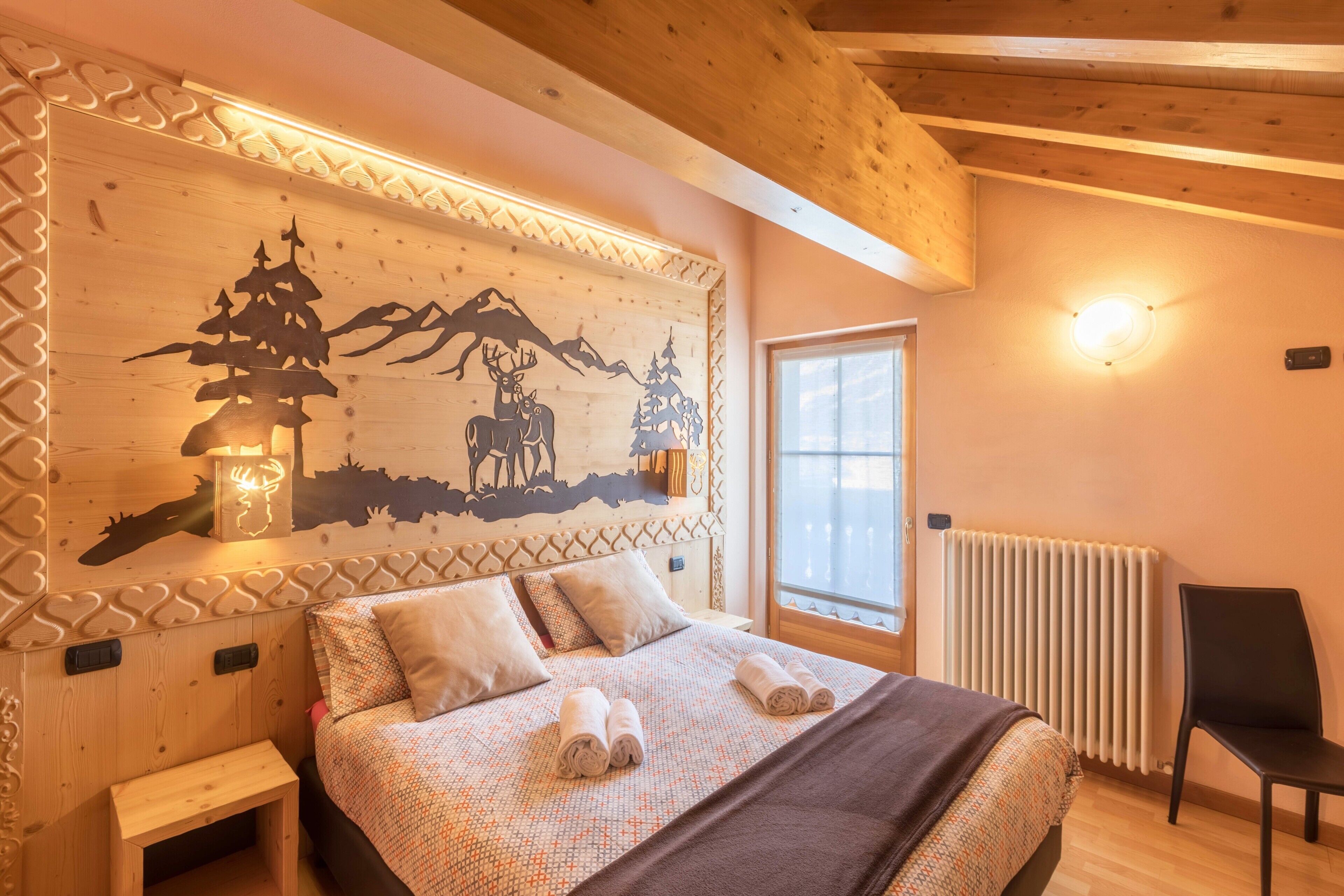 A wooden bedroom with a bed, pillows, a nightstand, a chair, a window, and a wall with a decorative design.