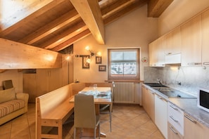 A cozy kitchen with wooden beams, a dining table set for two, and a window with a view.