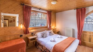 A wooden-paneled room with a bed, bedside tables, a bench, and a window with curtains. - Casa Azzurra Piano Terra with Mountain View, Wi-Fi & Garden; Parking Available (Livigno (SO))
