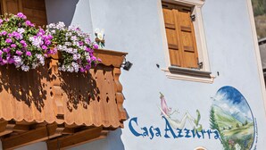 A building with a wooden balcony, a window, and a painted sign with a landscape. - Casa Azzurra Piano Terra with Mountain View, Wi-Fi & Garden; Parking Available (Livigno (SO))