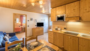 A wooden interior with a sofa, dining table, kitchen area, and a TV. - Casa Azzurra Piano Terra with Mountain View, Wi-Fi & Garden; Parking Available (Livigno (SO))