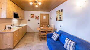 A compact kitchen with wooden cabinets, a dining table, and a blue sofa. - Casa Azzurra Piano Terra with Mountain View, Wi-Fi & Garden; Parking Available (Livigno (SO))
