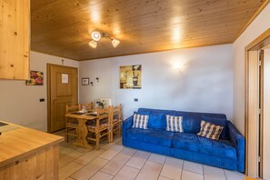 A room with a wooden ceiling, a blue sofa, a dining table with chairs, and a wooden cabinet.