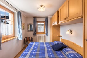Un dormitorio con cama, una ventana con cortinas, un radiador, armarios de madera y una lámpara fijada a la pared.